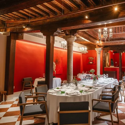 Salón elegante con paredes rojas, vigas de madera y mesas redondas vestidas con manteles blancos.