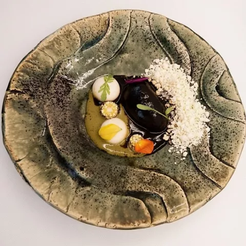 Plato creativo con salsa oscura, esferas y brotes presentado en vajilla artística.