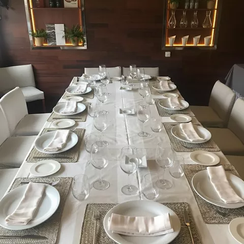 Mesa larga preparada con vajilla blanca y copas en comedor íntimo.