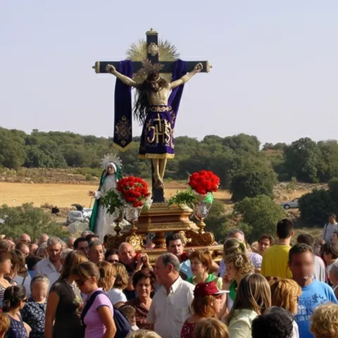 Multitud reunida alrededor de un paso con crucifijo y flores en un camino rural.