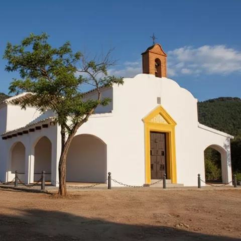 Ermita blanca con pórtico y puerta amarilla junto a un árbol