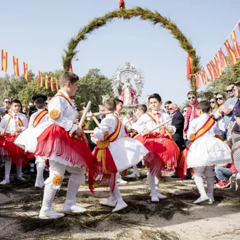 Niños con trajes tradicionales bailando con palos durante una fiesta popular al aire libre.