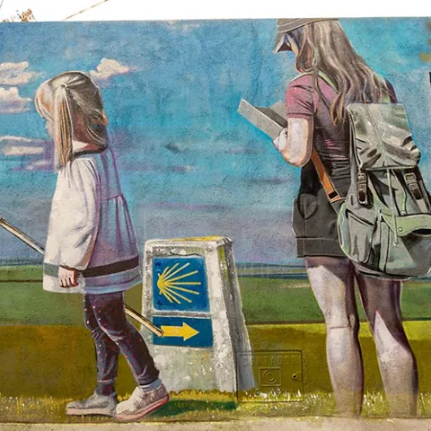 Mural de niña y mujer junto a señal de camino con concha amarilla.