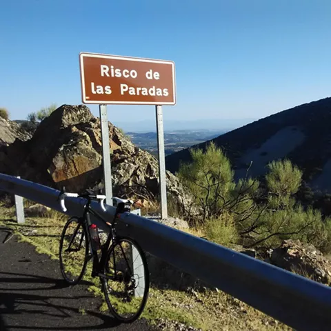 Bicicleta junto a una señal marrón en una carretera de montaña con valle al fondo.