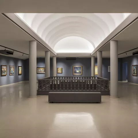 Sala de exposición con columnas y cuadros en paredes oscuras