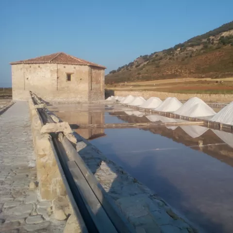 Canal de agua salina con pilas de sal y casa de piedra.