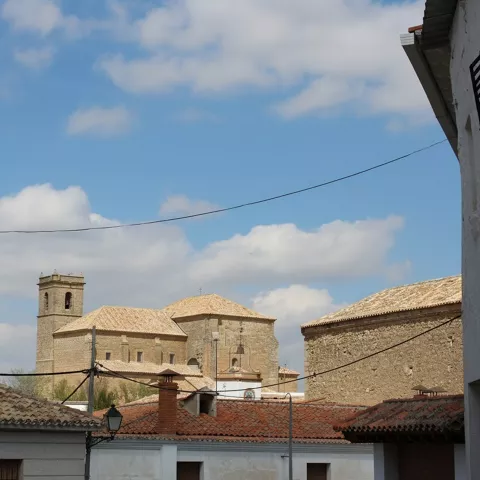 Una vista de la torre de una iglesia y tejados de casas desde una calle estrecha, bajo un cielo nublado.
