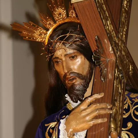 Detalle de rostro y manos de imagen religiosa abrazando una cruz.