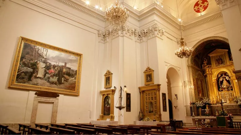 Interior de iglesia con bancos de madera, altares dorados y lámparas colgantes.