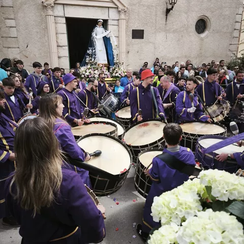 Grupo de tamborileros vestidos de morado tocando frente a una iglesia.