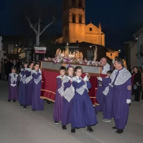 Procesión nocturna con niños vestidos de morado portando pequeño paso religioso.