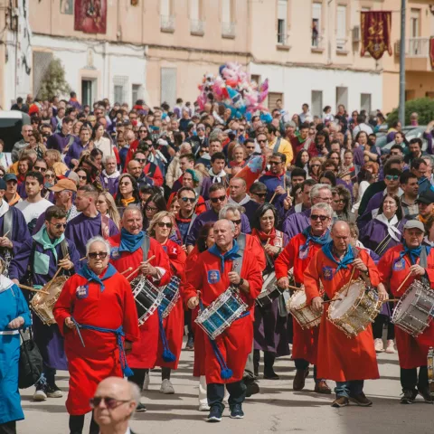Desfile con tamborileros vestidos de rojo avanzando por la calle.
