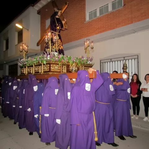 Grupo de cofrades con túnicas moradas portando un paso con figura y candelabros.