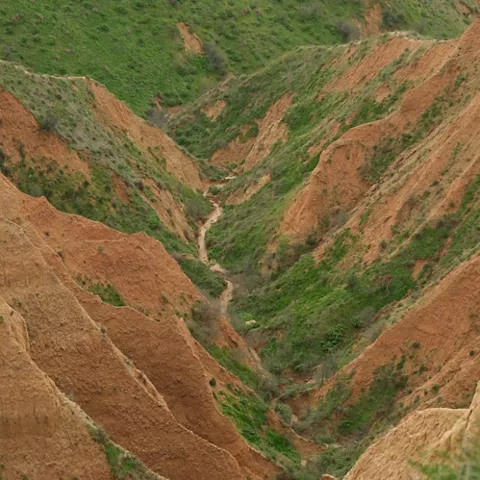 Cañón erosionado con laderas rojizas y un cauce seco en el fondo.