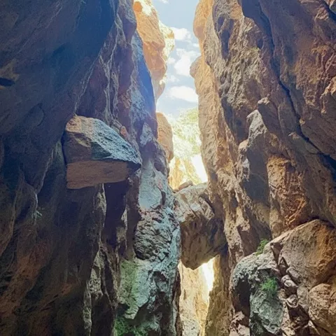 Paso estrecho entre paredes rocosas con grandes bloques y luz cenital.
