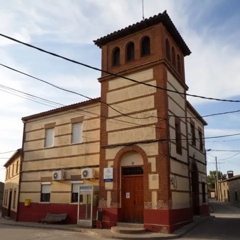 Un edificio de dos pisos con una torre cuadrada, construido con una mezcla de ladrillo y revoque, situado en la esquina de una calle de pueblo.
