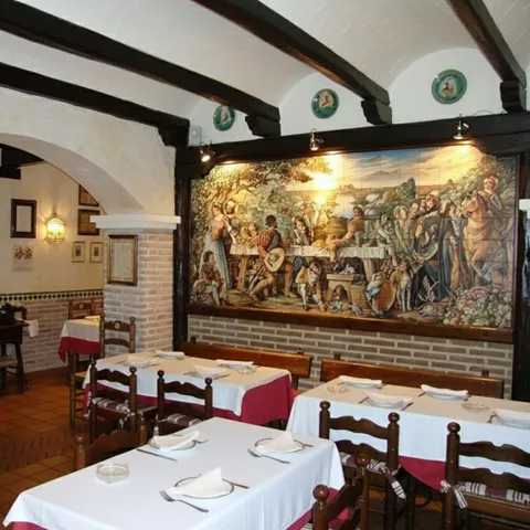 Comedor acogedor con mural cerámico y mesas con manteles blancos.