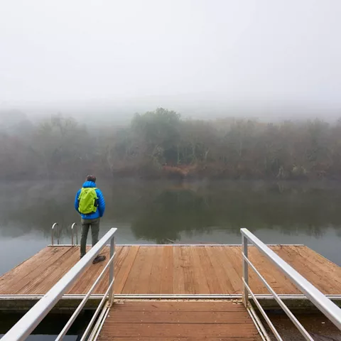 Persona observando el río desde embarcadero con niebla