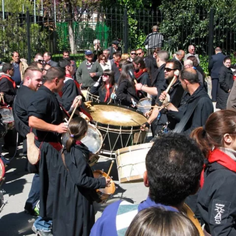 Grupo de tamborileros y público en un parque, con un gran bombo en el centro.