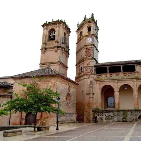 Conjunto monumental de piedra con dos torres, arcos porticados y plaza empedrada en primer plano.