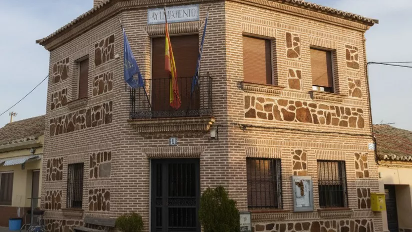 Fachada de un ayuntamiento de ladrillo con detalles de piedra irregular con banderas en el balcón.