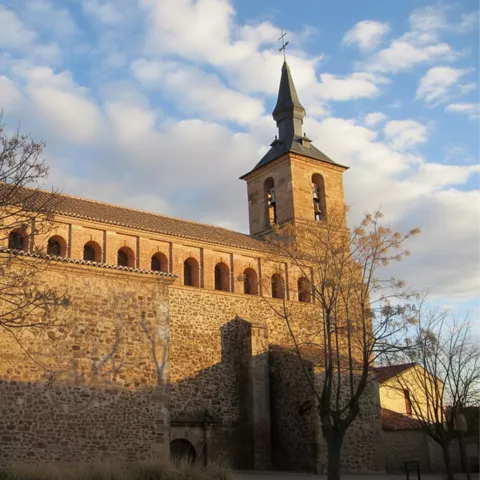 Vista lateral de iglesia de piedra con torre y arbolado