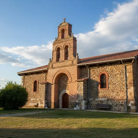Ermita rural construida con mampostería de piedra y una espadaña de ladrillo de tres niveles para campanas, situada en un prado verde.