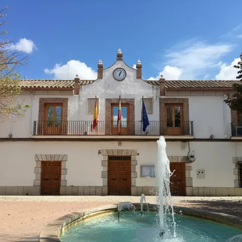 Fachada de edificio institucional con reloj, banderas y fuente frontal
