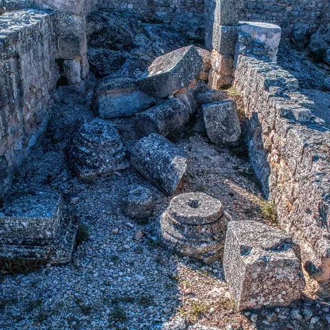 Ruinas de muros antiguos con bloques de piedra caídos en el suelo.