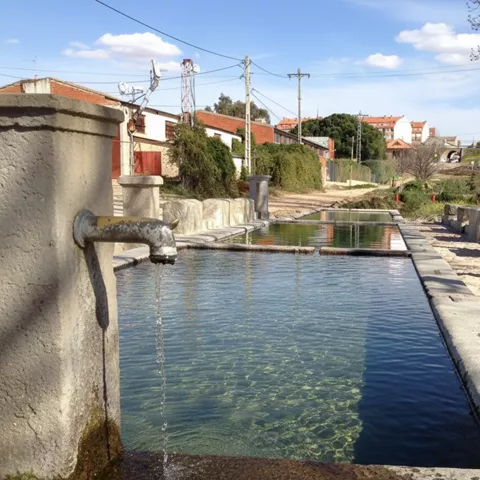 Un antiguo lavadero público de piedra con varios pilones rectangulares llenos de agua clara, bajo un cielo despejado.