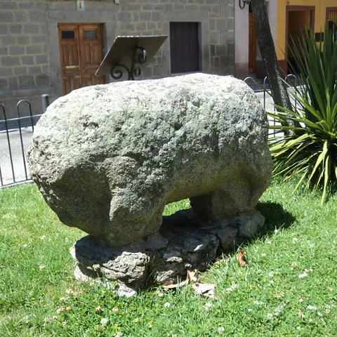 Escultura zoomorfa de piedra vista desde un lateral, con base de roca.