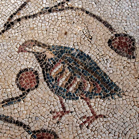 Detalle de mosaico antiguo con figura de ave sobre fondo geométrico.