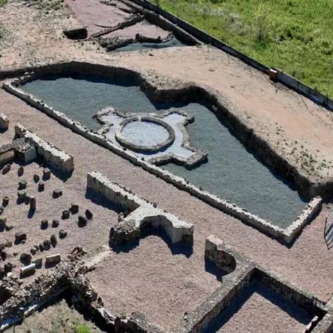 Vista aérea de complejo arqueológico con estanque rectangular y cimientos visibles.