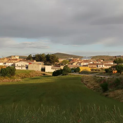 Paisaje rural de Villavaliente con casas bajas, campos verdes y suaves colinas bajo cielo nublado.