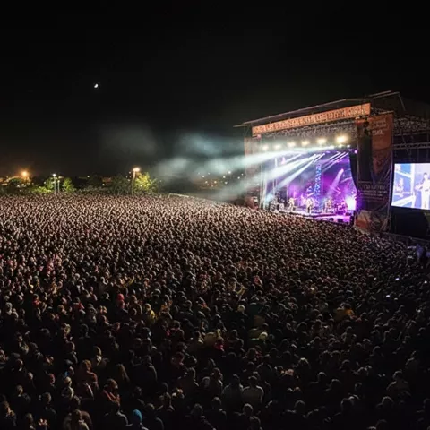 Multitud masiva frente a un escenario iluminado durante un concierto nocturno.