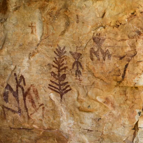 Pinturas rupestres con figuras humanas y símbolos en roca.