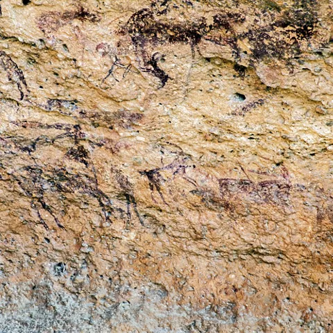 Pinturas rupestres de animales en una pared de roca, en tonos oscuros.