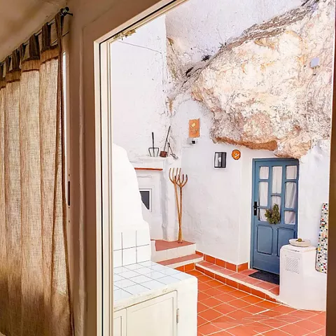 Entrada interior a vivienda excavada en roca con suelo de baldosas y puerta azul.