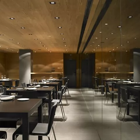 Sala de comedor moderna con mesas negras, iluminación cálida y paredes de madera.