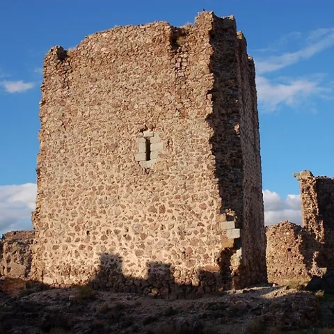 Torre de piedra en ruinas sobre terreno elevado con cielo azul al fondo.