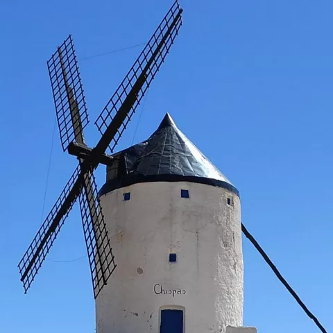 Camino de tierra que conduce a un molino de viento con aspas negras.