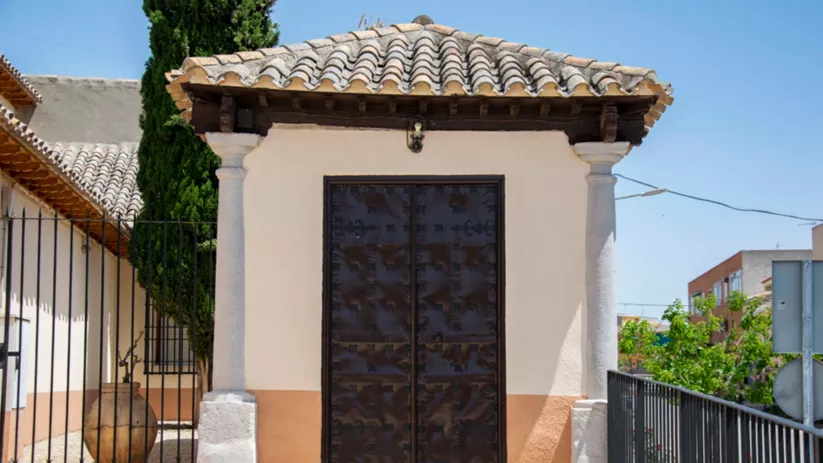 Fachada de capilla con puerta metálica y tejado de teja