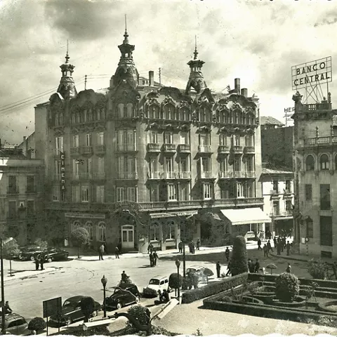 Imagen histórica en blanco y negro de plaza urbana con edificio emblemático y peatones.