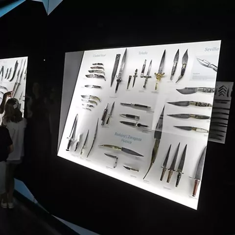 Personas observando vitrinas con cuchillos históricos en una exposición oscura.