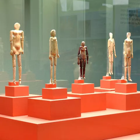 Vitrina con pequeñas figuras antiguas sobre pedestales y cerámica decorativa.