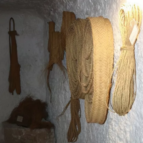 Herramientas y rollos de fibra vegetal colgados en pared encalada de cueva.