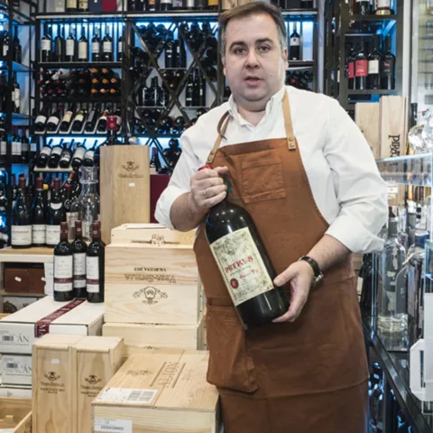 Hombre con delantal sostiene una botella grande de vino en una vinoteca.