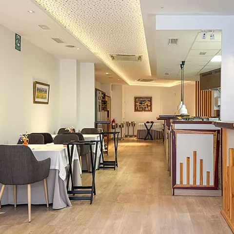 Vista del comedor con mesas alineadas y zona de servicio al fondo.