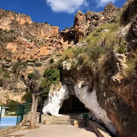 Entrada a cueva excavada en roca junto a sendero pavimentado.