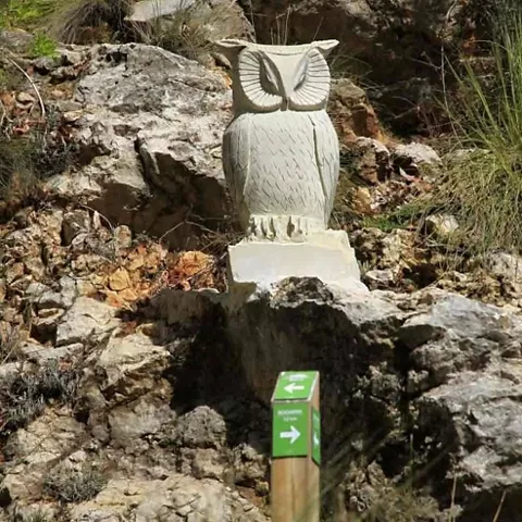 Escultura de búho tallada en piedra junto a una señal de sendero.